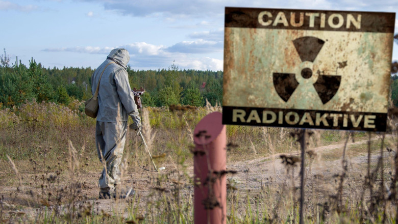 Military dosimetrist measures the radiation area, a sign with the inscription: caution, radiation, chemical protective suit and gas mask.