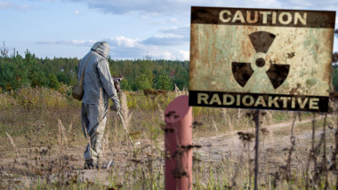 Military dosimetrist measures the radiation area, a sign with the inscription: caution, radiation, chemical protective suit and gas mask.