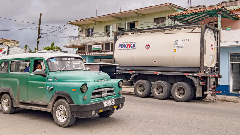 An old American car drives past a truck belonging to a private Cuban company (mipyme) parked in front of a gas station with an IsoTank of imported fuel in Havana on March 19, 2026