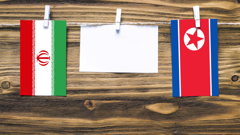 Hanging flags of Iran and North Korea attached to rope with clothes pins with copy space on white note paper on wooden background.Diplomatic relations