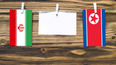 Hanging flags of Iran and North Korea attached to rope with clothes pins with copy space on white note paper on wooden background.Diplomatic relations