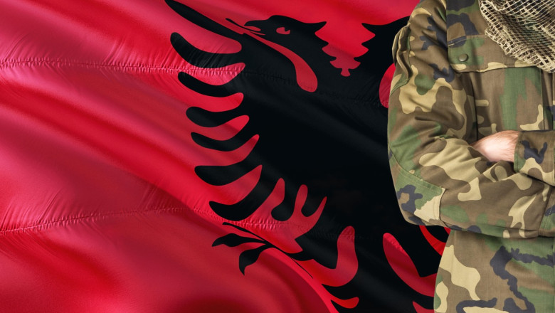 Crossed arms Albanian soldier with national waving flag on background - Albania Military theme.
