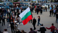 A man waves a Bulgarian flag while people perform a dance after a political rally