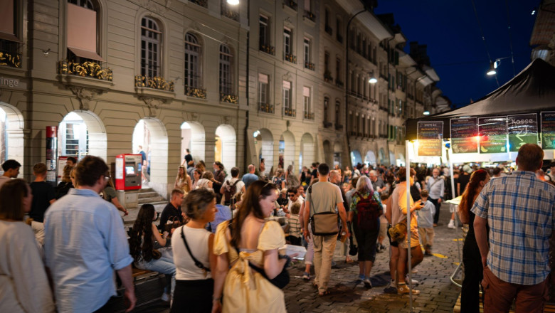 07-08-2025 Bern, Switzerland. Crowds of people enjoying the street food and performances of Buskers street music festival at night. Blue hour light, l