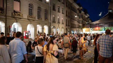 07-08-2025 Bern, Switzerland. Crowds of people enjoying the street food and performances of Buskers street music festival at night. Blue hour light, l