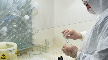 Scientist in protective white coat, mask and gloves analyzes a virus or bacteria sample in a laboratory with vials, glass flasks and chemicals