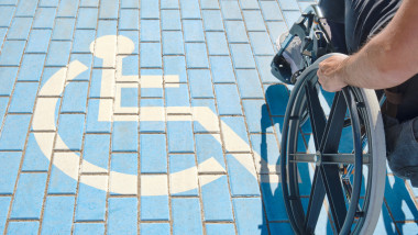 unrecognizable handicapped man in a wheelchair passing over handicapped sign painted on the ground