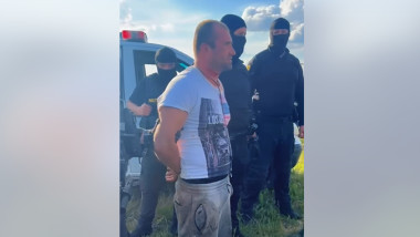 un barbat este incatusat si inconjurat de politisti mascati