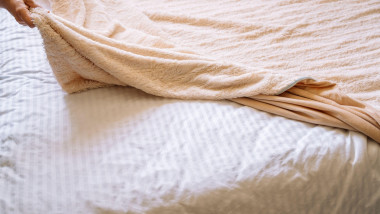 Woman pulling beige blanket over bed in bedroom