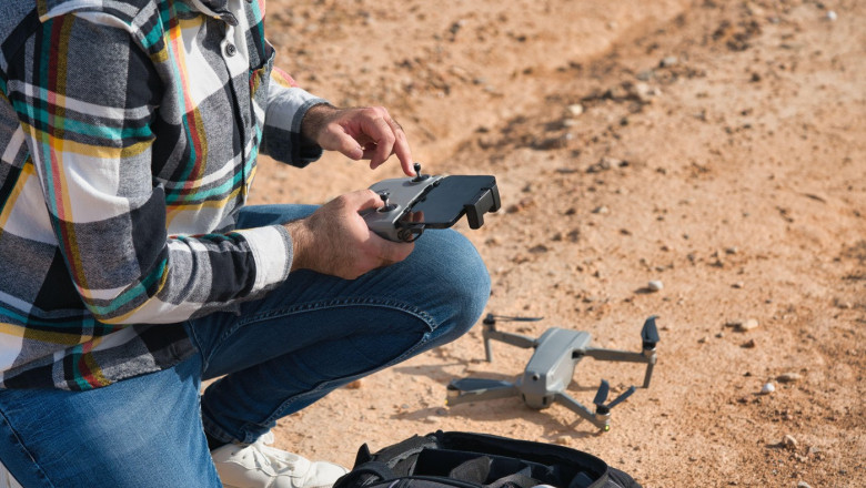 A man kneels on a dirt road, preparing a drone to fly