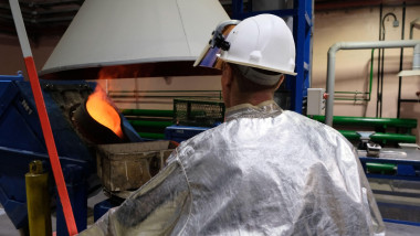 A worker in overalls watches the melting of metal and the casting of ingots.