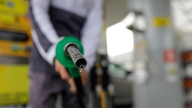 Shallow depth of field (selective focus) details with a man holding a fuel pump dripping with gasoline in a gas station.