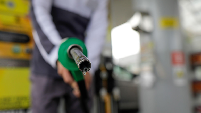 Shallow depth of field (selective focus) details with a man holding a fuel pump dripping with gasoline in a gas station.