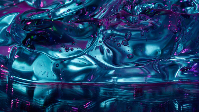 Close-up abstract composition of translucent turquoise ice cubes with trapped bubbles, illuminated by vivid magenta and blue reflections for a cool, g