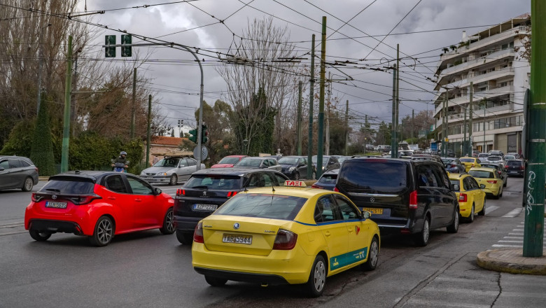 Traffic congestion in Athens, Greece. Yellow taxis and private cars wait at an intersection below an intricate network of overhead public transport wi