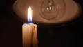 Burning candle near a switched off light bulb in complete darkness.