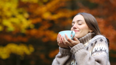 Happy woman in autumn smelling coffee in a park