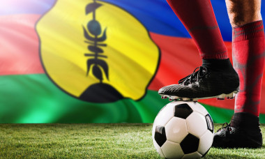 Close up legs of New Caledonia football team player in red socks, shoes on soccer ball at the free kick or penalty spot playing on grass.