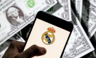 In this photo illustration Spanish professional football club team Real Madrid Club de Ftbol commonly known as Real Madrid logo seen on an Android mobile device screen with the currency of the United States dollar icon, $ icon symbol in the background.