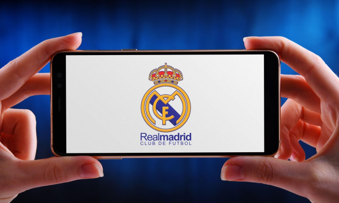 POZNAN, POL - JUN 20, 2020: Hands holding smartphone displaying logo of Real Madrid, a Spanish professional football club based in Madrid