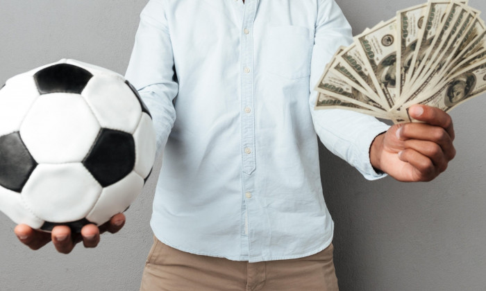 Happy smiling african man showing football and money banknotes isolated over gray background