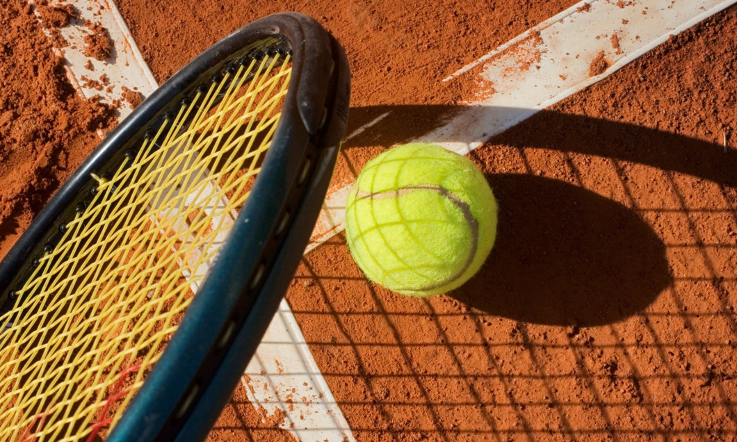 A tennis ball with details of a racquet , shadows and a clay court