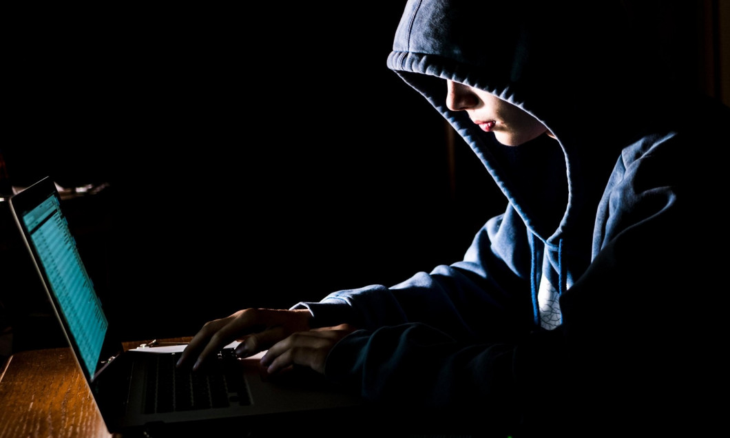 anonimous man in the hoodie in dark studio typing text online on the internet with copy space