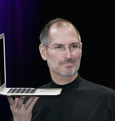 steve jobs, cofondatorul apple, cu un laptop in mana in timpul unei prezentari