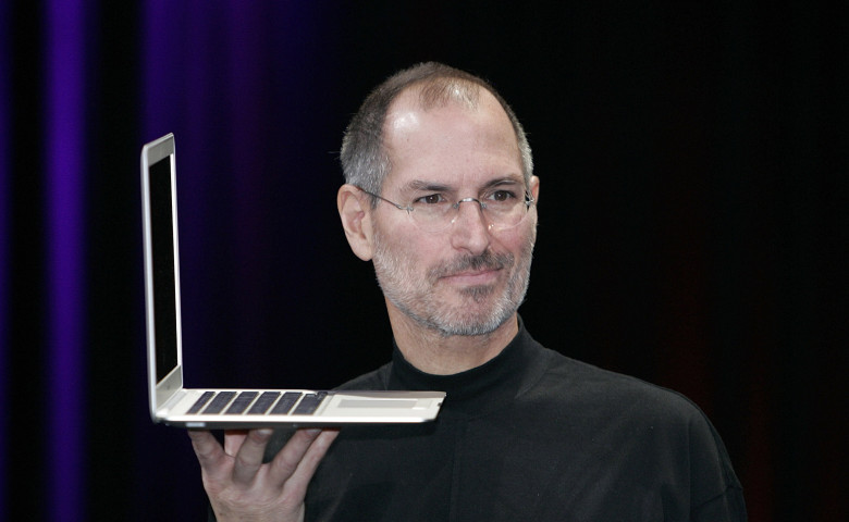 steve jobs, cofondatorul apple, cu un laptop in mana in timpul unei prezentari