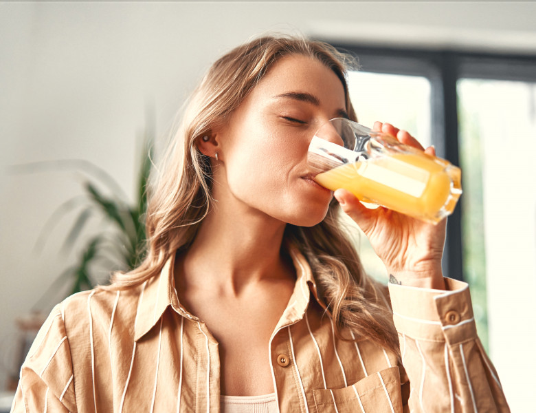 A,Young,Happy,Woman,Standing,In,The,Kitchen,Drinks,Orange