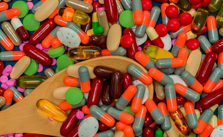 Pile of colorful pills and wood spoon. Medicine, vitamins, supplement and minerals. Antibiotics drug resistance and drug use with reasonable concept.