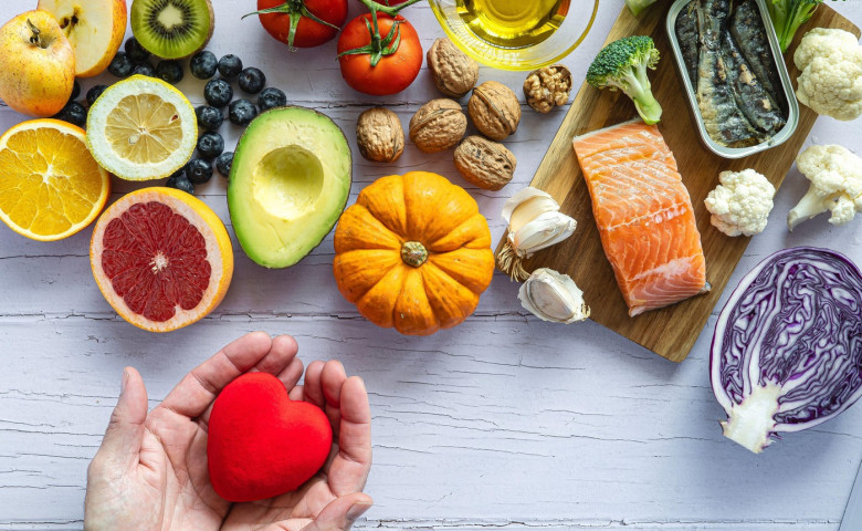 Two hands holding a red heart surrounded by healthy foods to prevent cancer and heart disease. Fresh fruits, vegetables and fish. Disease prevention.