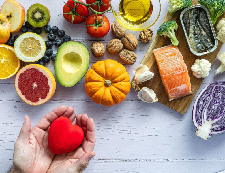 Two hands holding a red heart surrounded by healthy foods to prevent cancer and heart disease. Fresh fruits, vegetables and fish. Disease prevention.