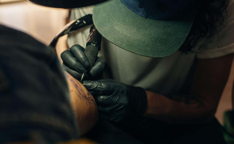 Close up of professional tattooer artist doing picture on hand of man by machine black ink from a jar.