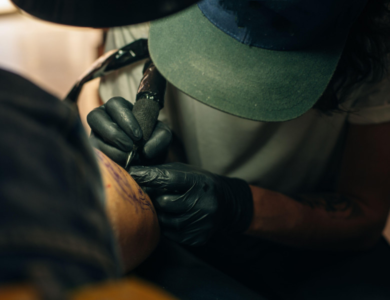 Close up of professional tattooer artist doing picture on hand of man by machine black ink from a jar.