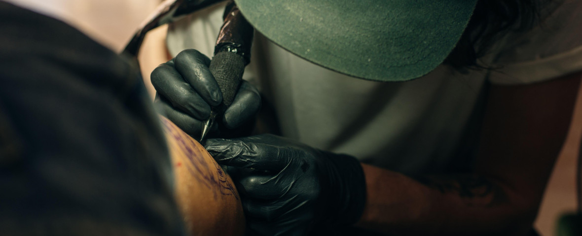 Close up of professional tattooer artist doing picture on hand of man by machine black ink from a jar.
