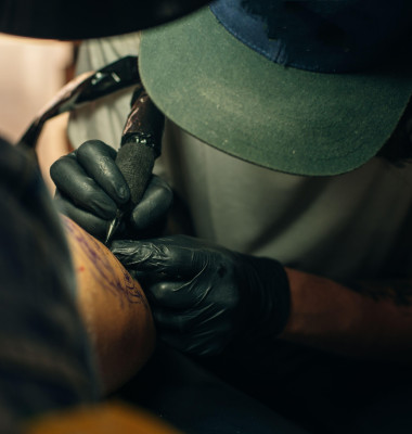 Close up of professional tattooer artist doing picture on hand of man by machine black ink from a jar.