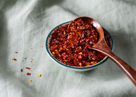 Bowl of crushed red pepper flakes with a wooden spoon on green linen fabric