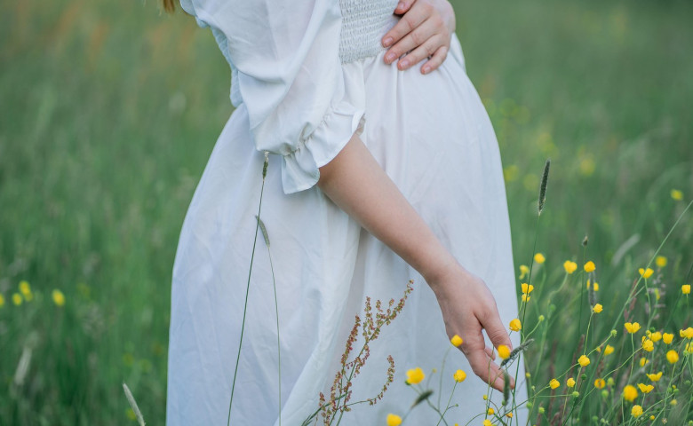 Pregnant young woman holds her hands on her belly, walking in the field in anticipation of the baby. Happy motherhood.