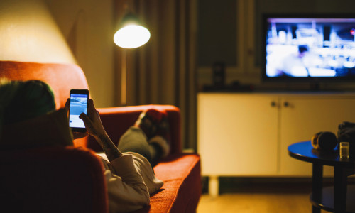 Femeie se uită la telefonul mobil în timp ce merge televizorul