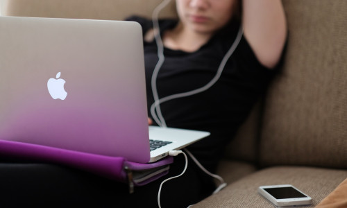Tipă stă pe canapea, sedentară și ascultă muzică la laptop Mac, gadget, divertisment