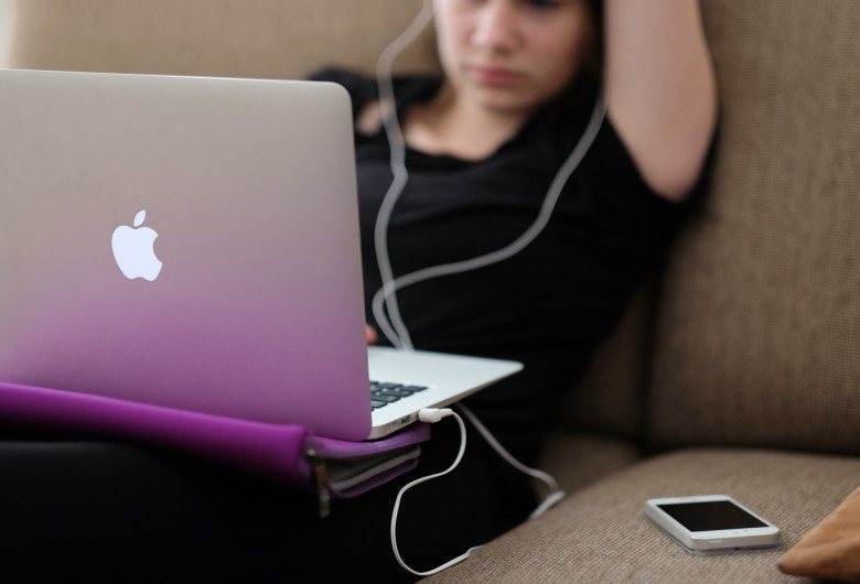 Tipă stă pe canapea, sedentară și ascultă muzică la laptop Mac, gadget, divertisment