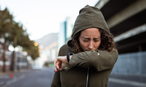 Caucasian woman coughing and wearing a smartwatch in the streets