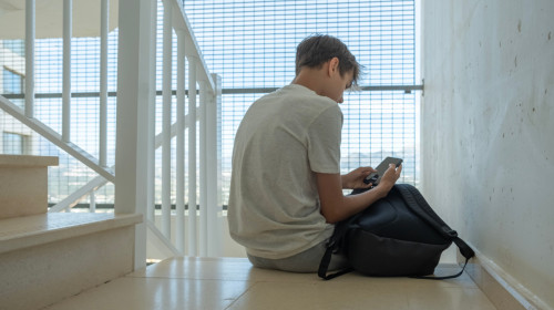 Sad,Teenage,Boy,With,Mobile,Phone,And,Backpack,Sitting,On