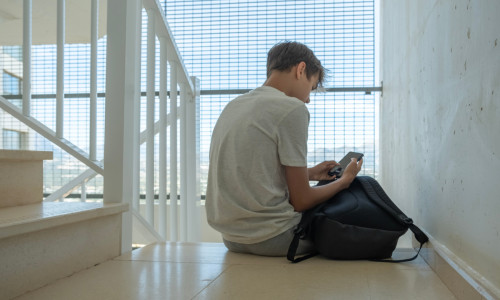 Sad,Teenage,Boy,With,Mobile,Phone,And,Backpack,Sitting,On
