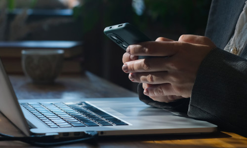 Businesswoman,Uses,Smartphone,Sitting,At,Her,Desk.