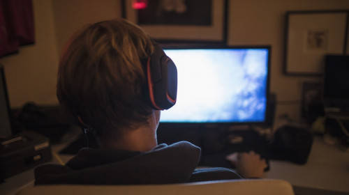 Teenage boy with headphones playing video game in dark bedroom