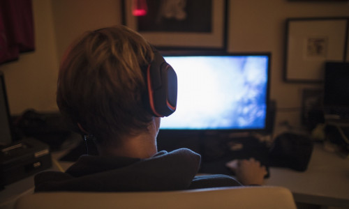 Teenage boy with headphones playing video game in dark bedroom