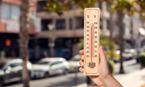 Hot,Weather.,Thermometer,In,Hand,In,Front,Of,An,Urban
