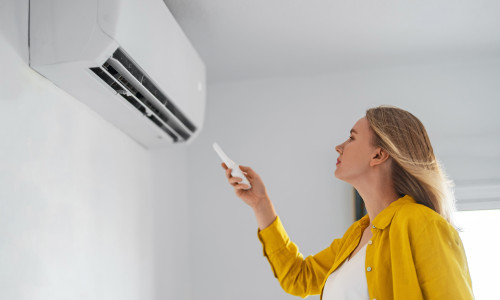 Woman,Holding,Remote,Control,Aimed,At,The,Air,Conditioner.